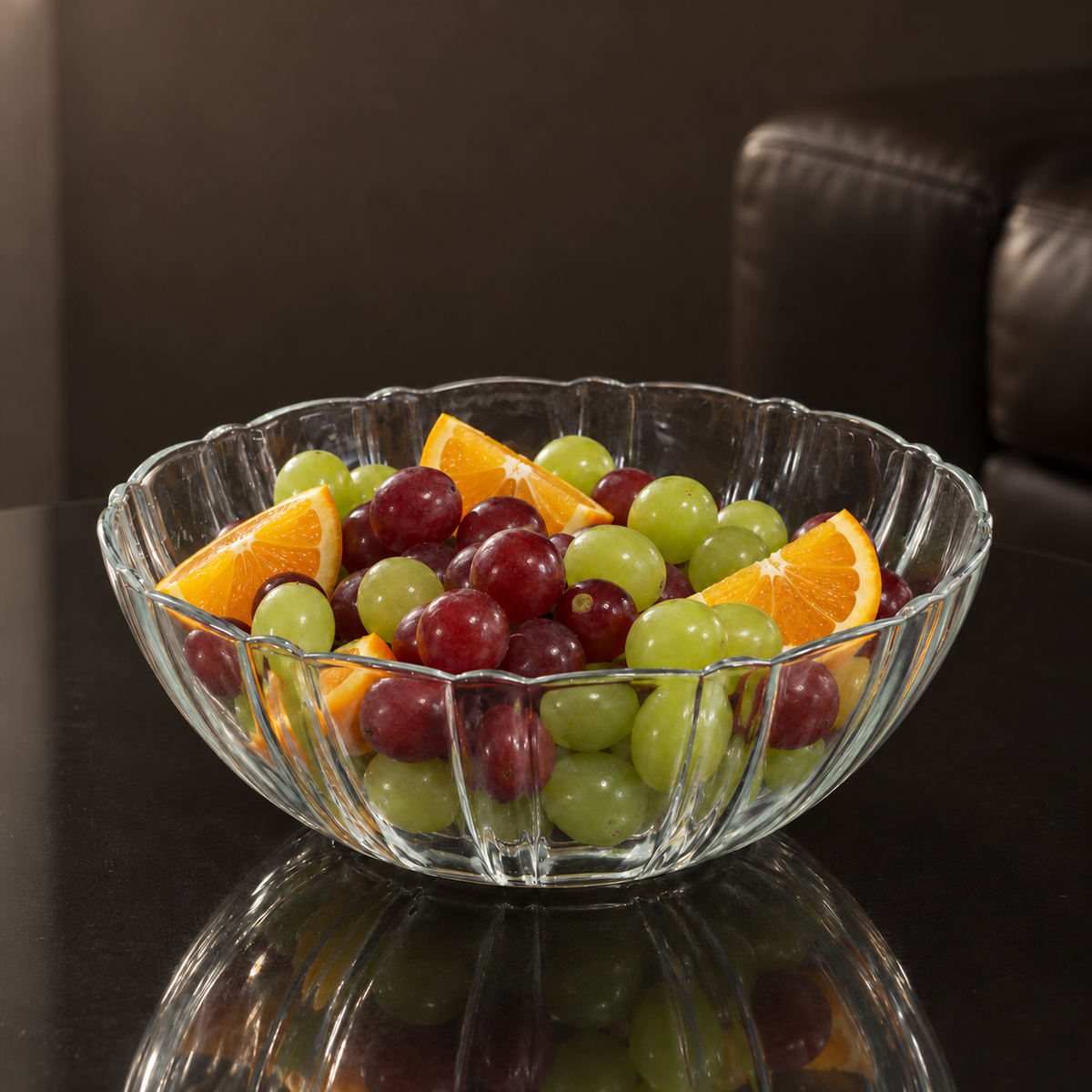 Fluted glass bowl with grapes and oranges on a black table